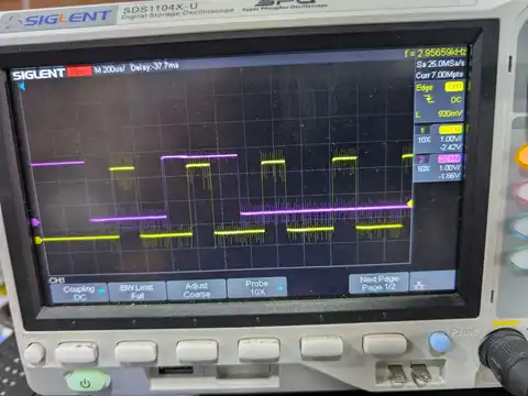 A Siglent SDS1104X-U oscilloscope on the bench, its screen showing the clock and command lines of an eMMC flash chip during power-up initialisation: steady levels broken by dense bursts of fast pulses on the yellow and magenta traces.