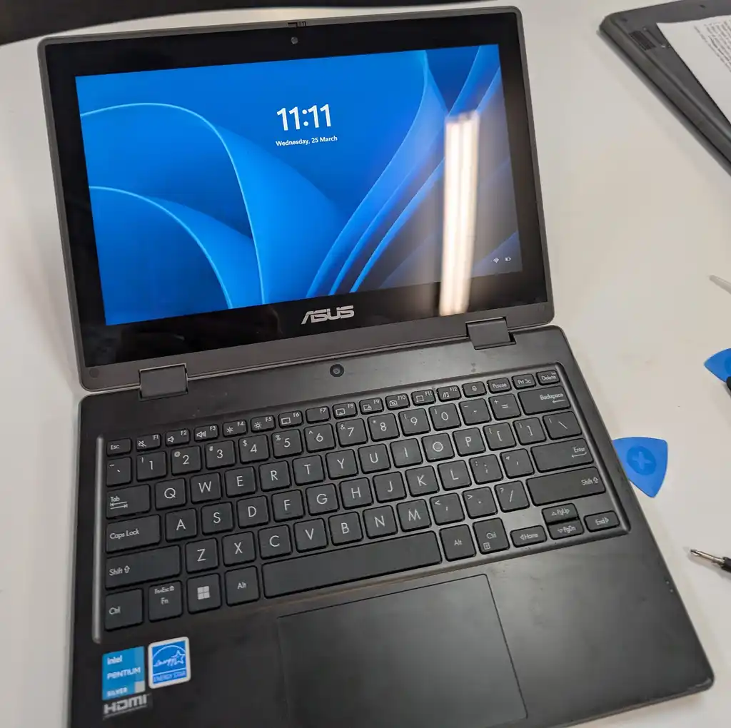 The same ASUS 2-in-1 convertible laptop after the screen replacement, open on the bench and running with a clean, undamaged display.