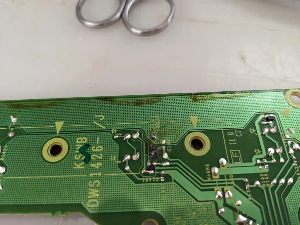 Close-up of the reworked solder joints on the Pioneer CDJ control board, with brown staining from the liquid damage across the board edge.