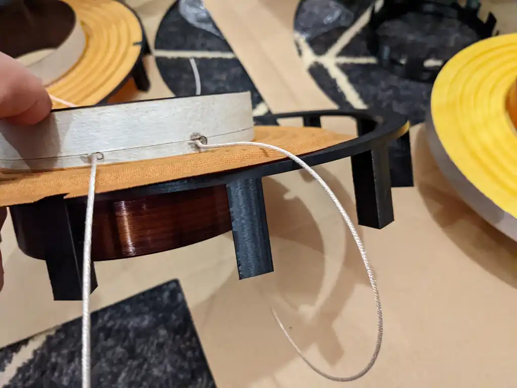 A replacement voice coil for the Precision Devices PD186 on its former, held in the custom 3D-printed jig, with the tinsel lead being dressed before assembly.
