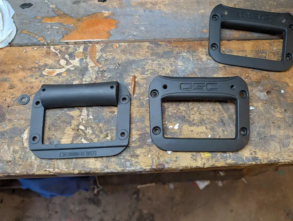 Three of the QSC speaker's own handles, stripped and repainted, laid out on the workbench ready to be refitted.